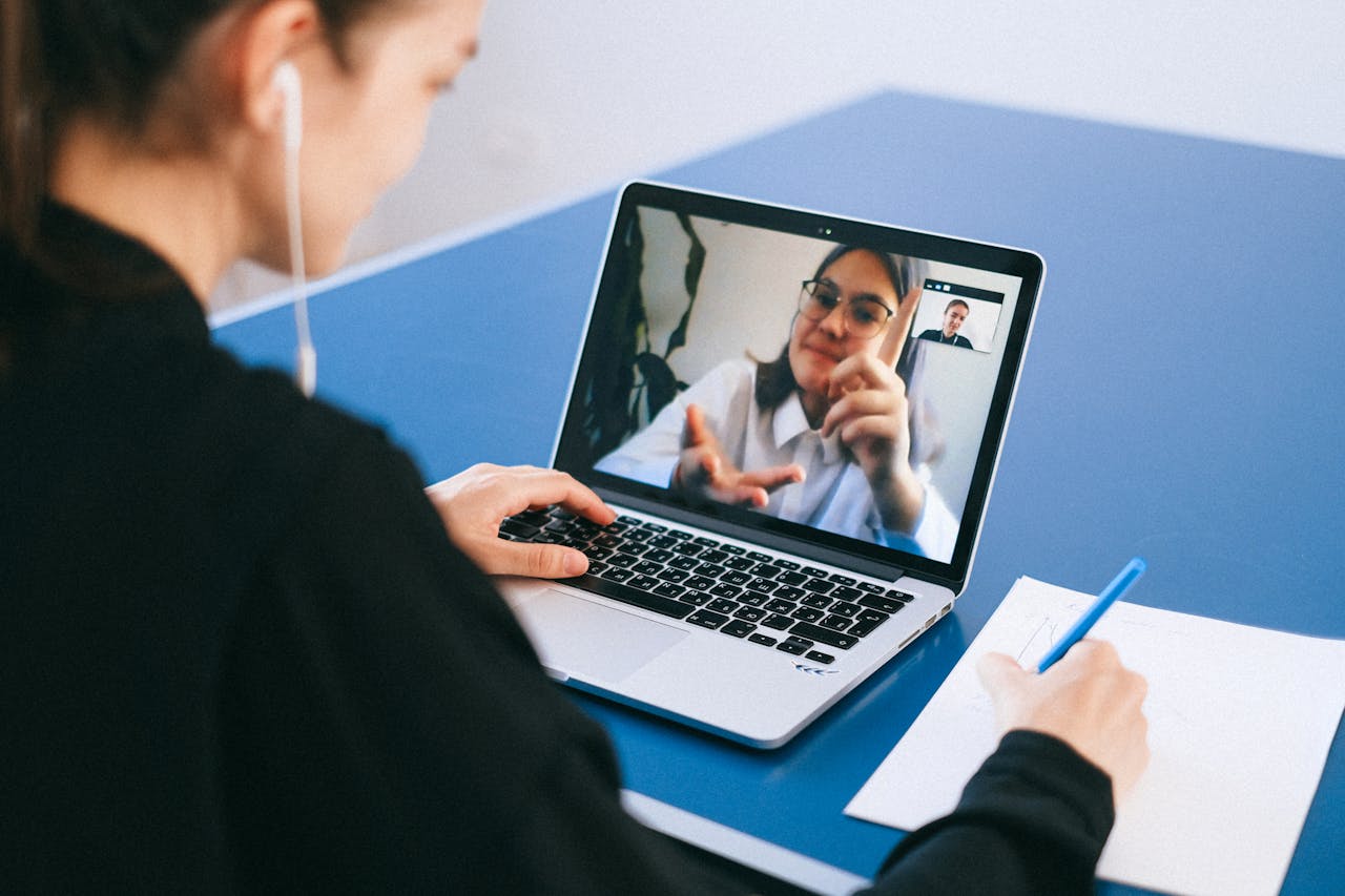 Crafting Captivating Headlines: Your awesome post title goes here Woman participating in a virtual meeting, taking notes during a video conference on a laptop.